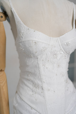 A luxurious lace mini dress with a corset base and hand-finished pearls, creating a festive and refined silhouette